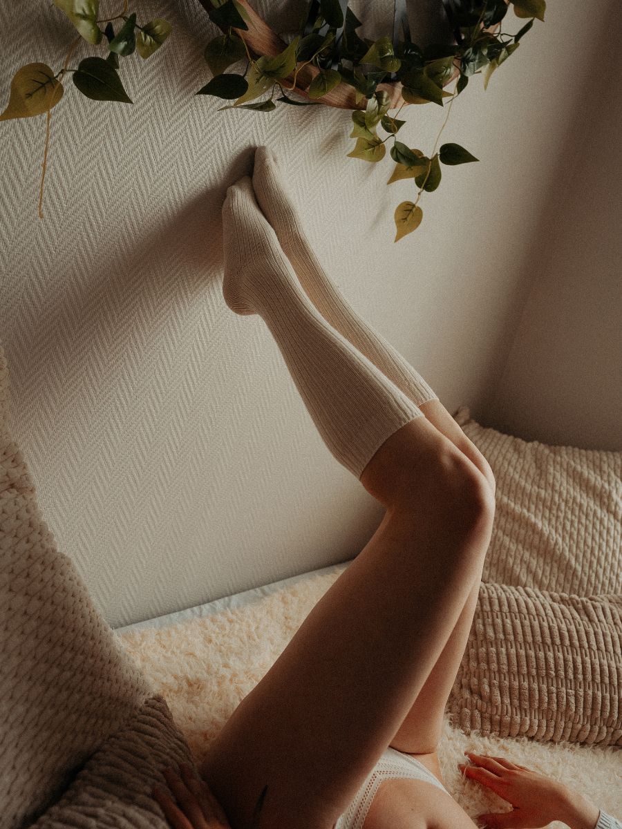 Portrait boudoir en gros plan, jambes levées en chaussettes hautes contre un mur.