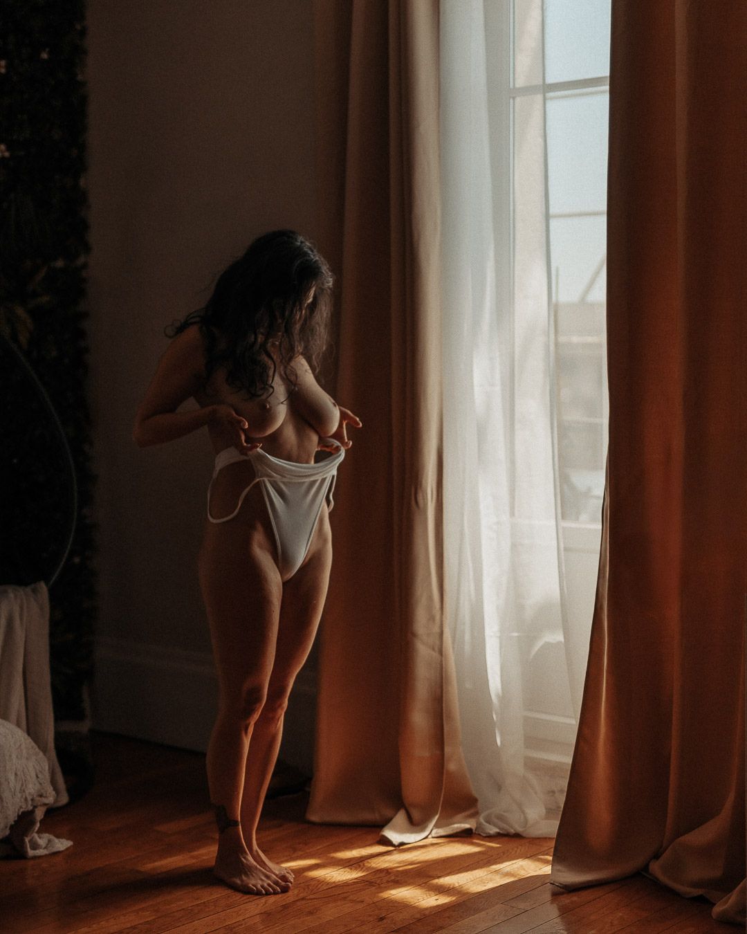 Portrait boudoir debout devant une fenêtre, lingerie blanche et lumière du jour.
